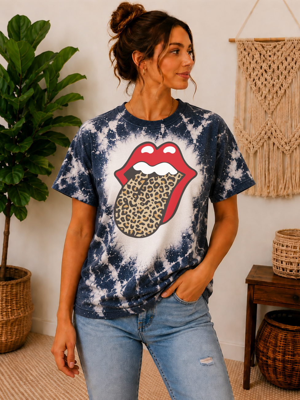 A woman wearing a blue and white tie-dye t-shirt with a large red lips and leopard print tongue graphic, paired with light-wash blue jeans in a styled indoor room setting.
