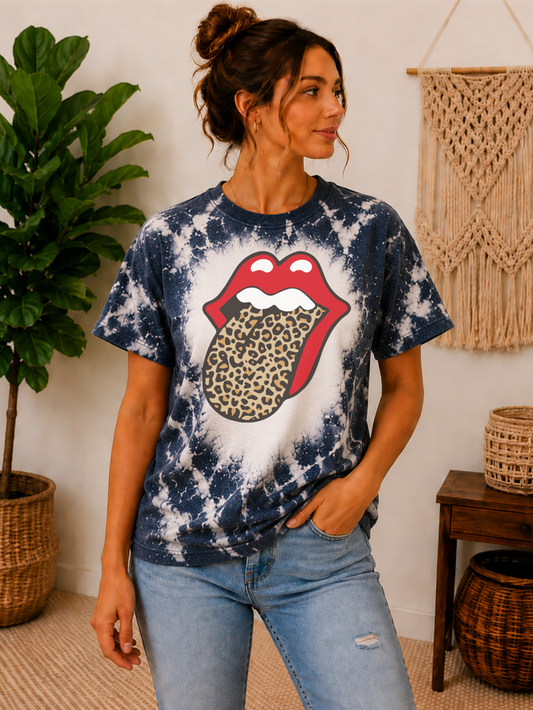 A woman wearing a blue and white tie-dye t-shirt with a large red lips and leopard print tongue graphic, paired with light-wash blue jeans in a styled indoor room setting.