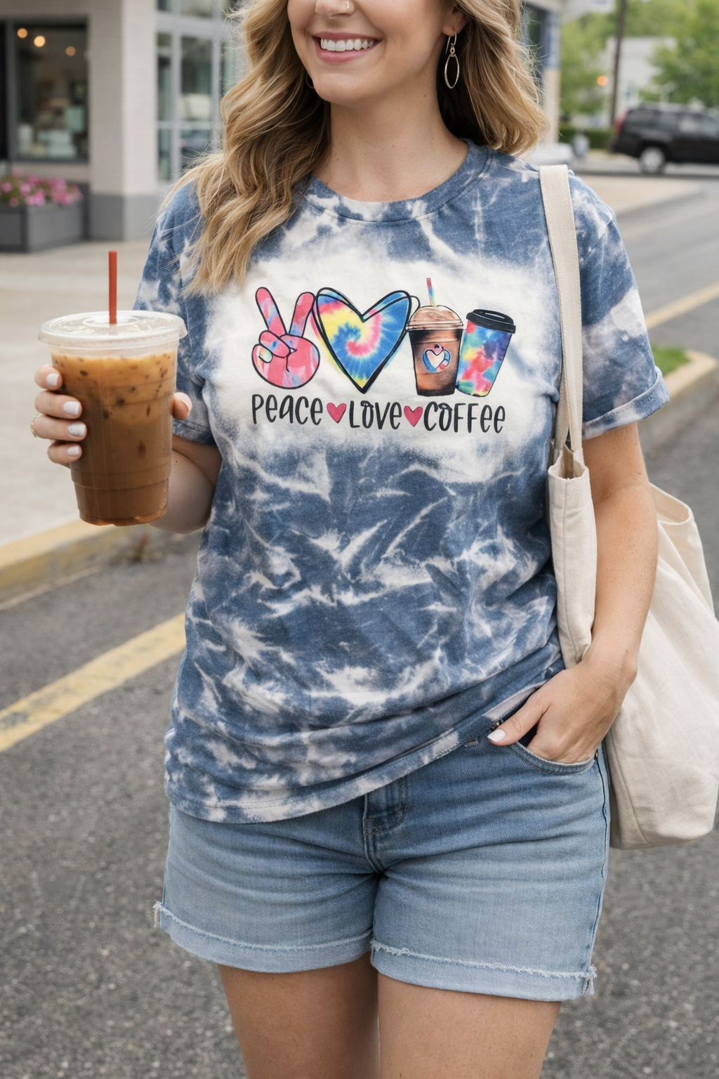 Woman wearing a tie-dye t-shirt with 'Peace Love Coffee' design, holding iced coffee.